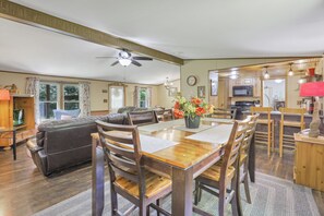 A spacious living room with a wooden dining table, leather sofa, and a kitchen area in the background.