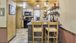 A kitchen with a wooden ceiling, a microwave, a stove, and two bar stools. - Redhead Hollow Cottage | Hocking Hills, Hot Tub (Rockbridge)