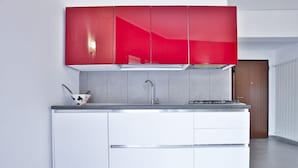 Une cuisine moderne avec des meubles blancs, une partie supérieure rouge, un évier en acier inoxydable et un petit saladier noir et blanc posé sur le plan de travail.