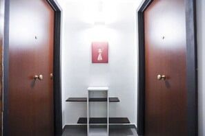 A hallway with two wooden doors, a white wall, and a small white table with three black shelves.