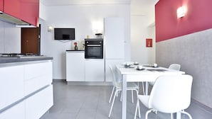 Une cuisine moderne avec des meubles blancs, un four noir et une table à manger entourée de chaises blanches.