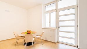 Ein Zimmer mit Esstisch, zwei Stühlen, einem Fenster mit Jalousien und einer Tür.