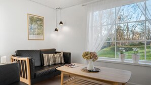 A modern living room with a black leather sofa, a wooden coffee table, and a large window with a view of a garden. - Awesome home in Korsør with WiFi (Korsør)