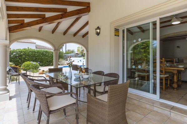 An outdoor patio with wicker furniture, a glass table, and a view of the backyard.
