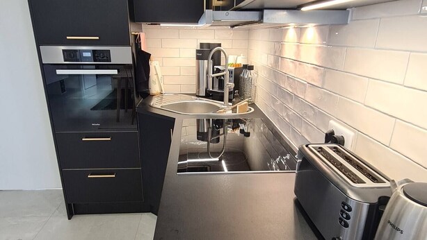Uma cozinha moderna com armários pretos, forno embutido, máquina de café, torradeira e chaleira.