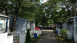 Une rangée de maisons mobiles entourées de clôtures blanches, une allée pavée et des arbres en arrière-plan.