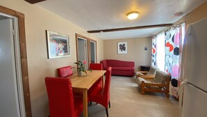 Un coin repas avec une table en bois et des chaises rouges, un canapé rouge et un fauteuil à motifs.