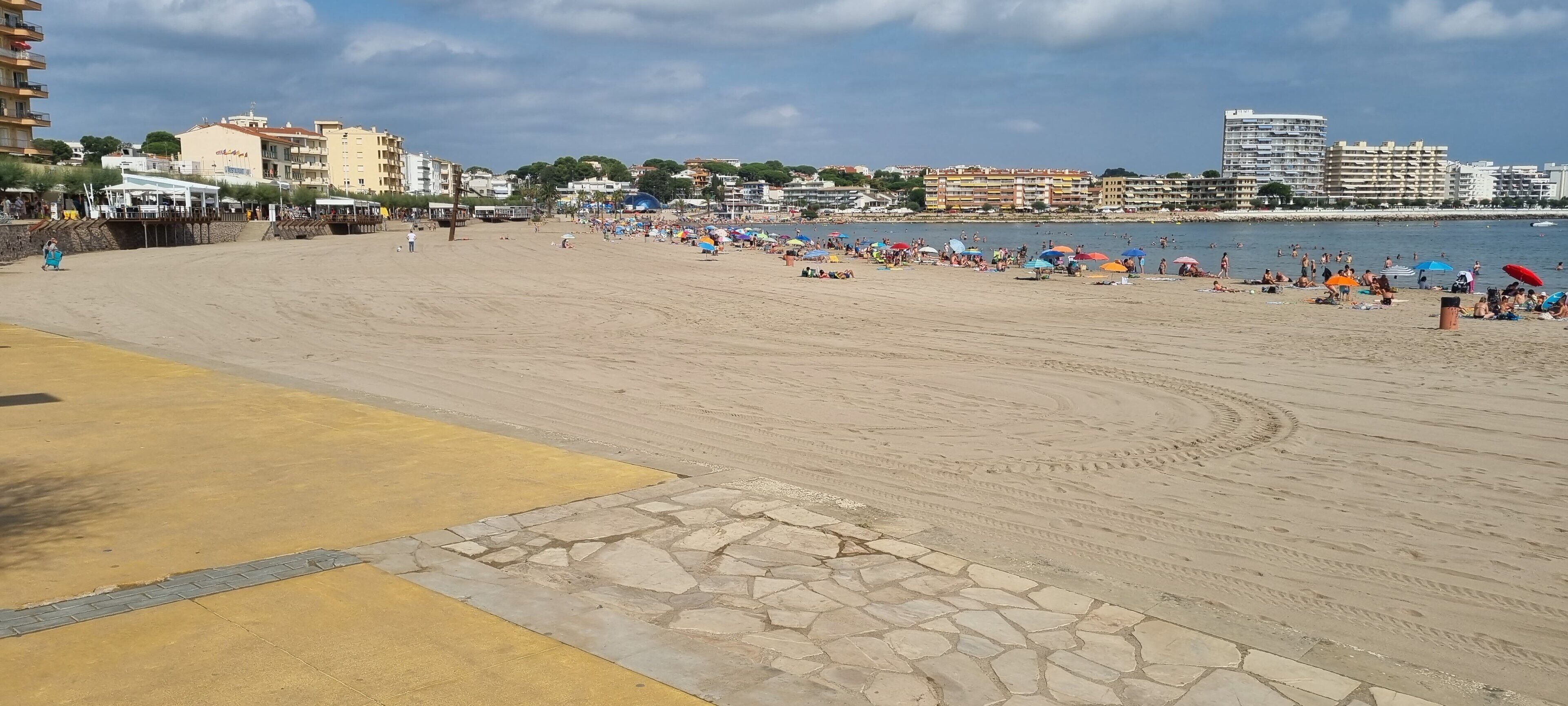 A beach with a paved walkway, beach umbrellas, and people.