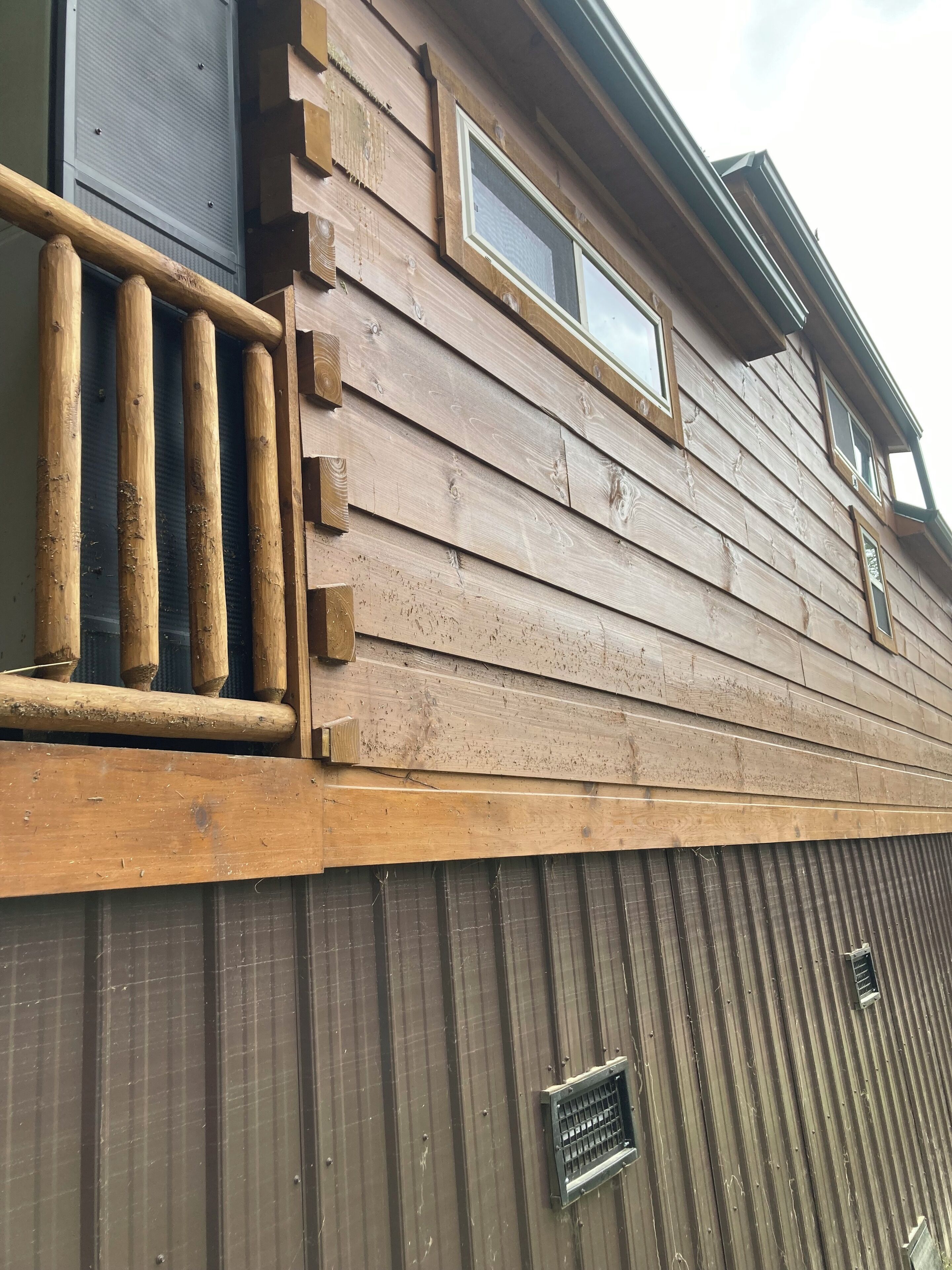 Une façade en bois avec un bardage horizontal, une grille d’aération en métal et une fenêtre ornée d’une grille métallique.