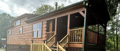 A wooden cabin with a deck and stairs leading to a covered porch.