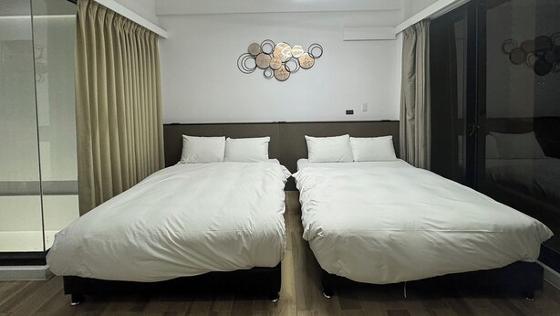 Une chambre d’hôtel moderne avec deux lits, une grande fenêtre avec des rideaux, un luminaire fixé au mur et une œuvre d’art décorative.