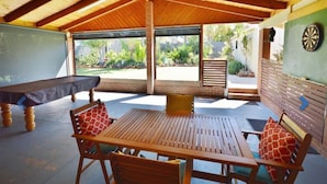 Un patio al aire libre con una mesa y sillas de madera, un dardo y una mesa de billar.