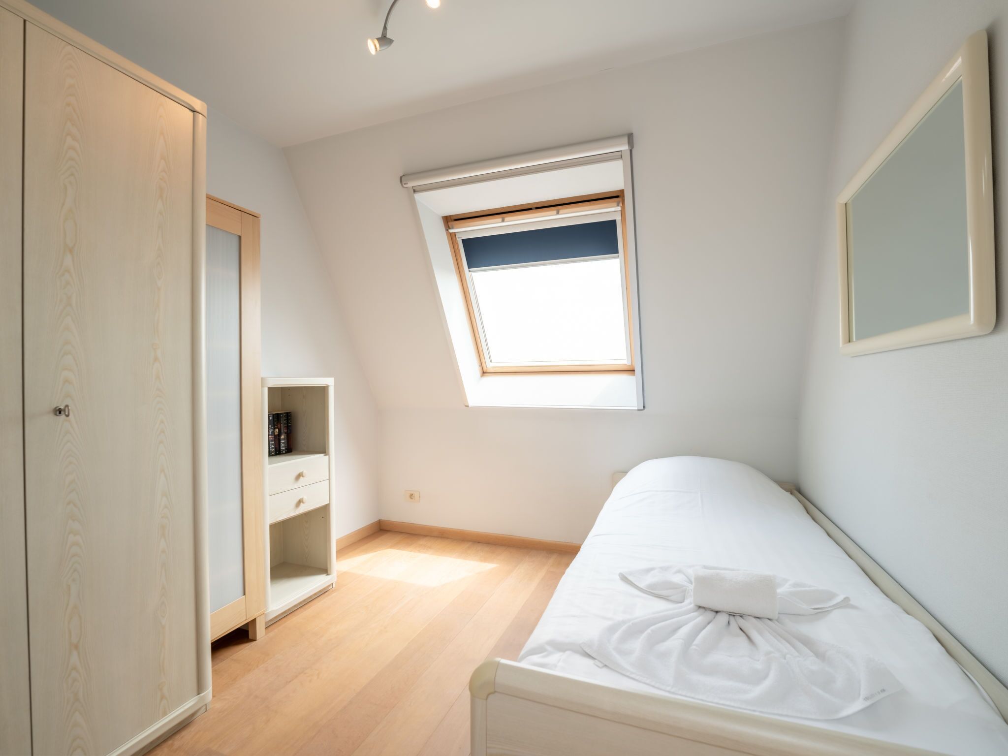 Ein Schlafzimmer mit einem Einzelbett, einem Kleiderschrank, einer kleinen Ablagefläche und einem Fenster mit Ausblick.