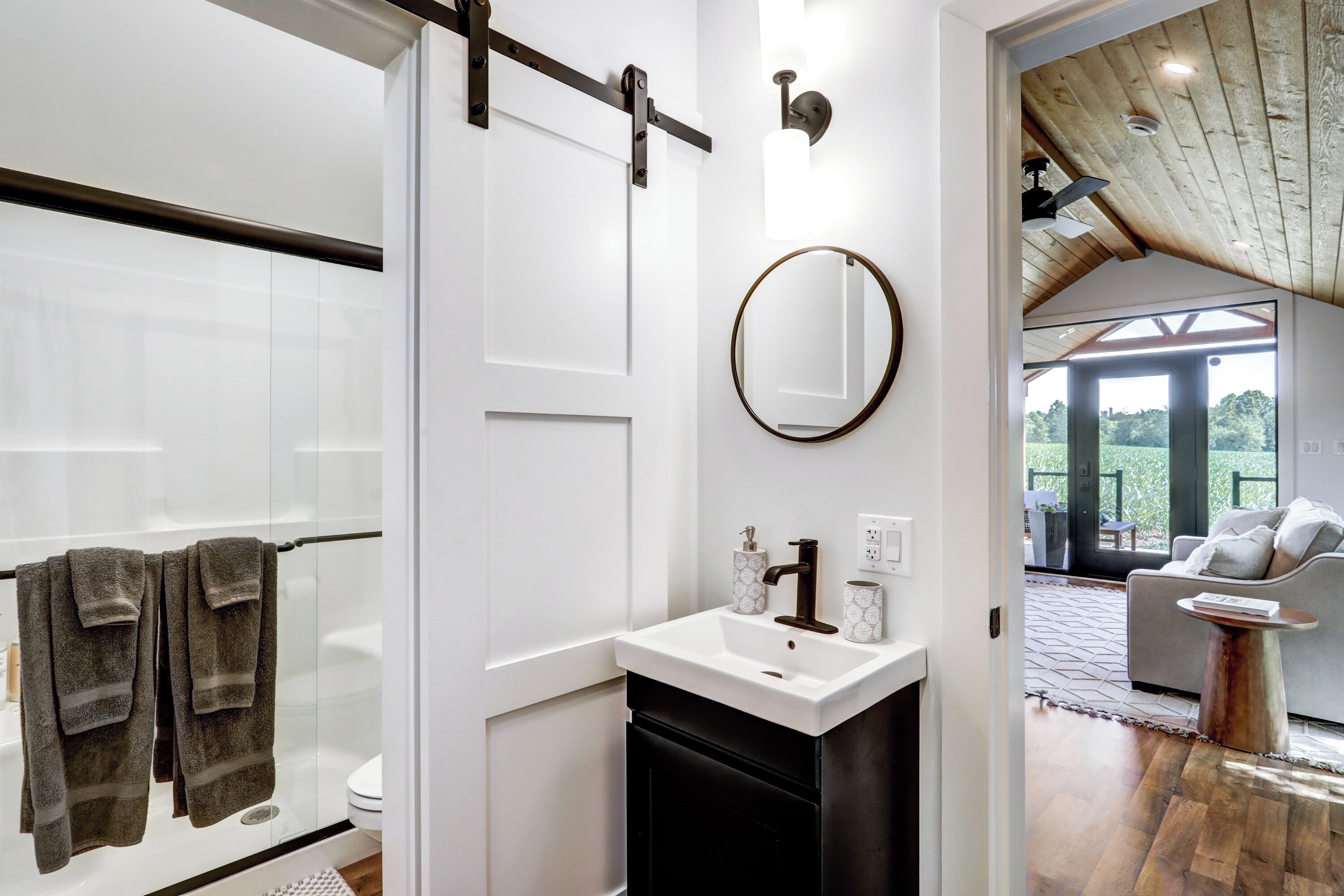 A modern bathroom with a glass shower, a white sink with a black faucet, and a round mirror.