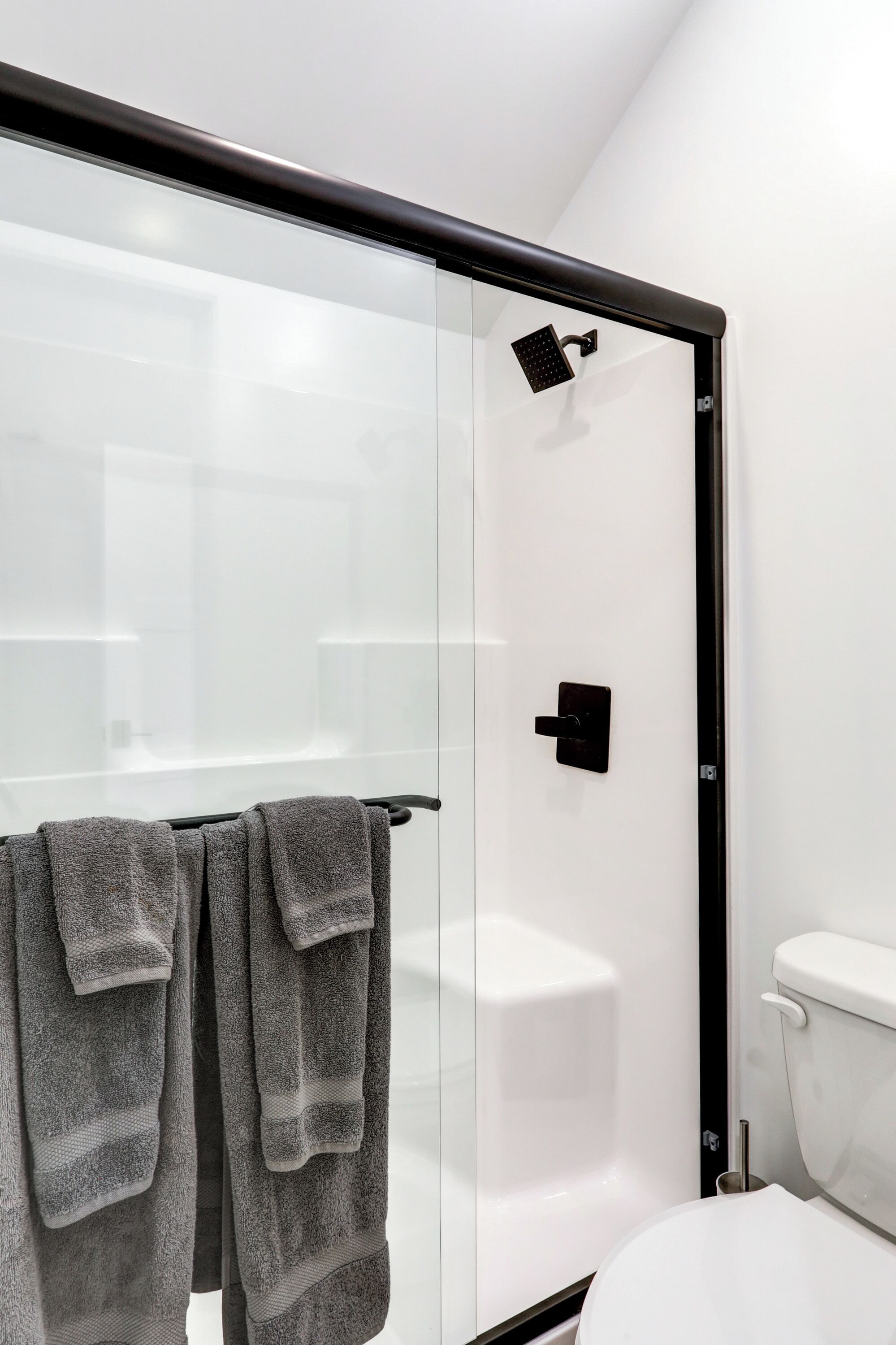 Un baño moderno con cabina de ducha de vidrio, inodoro y toallero con toallas.