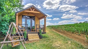 Una cabaña de madera con un porche, rodeada por un campo y árboles.