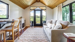 Una habitación acogedora con techo de madera, un sofá con cojines, una mesa de comedor con sillas y vistas al exterior a través de un ventanal.