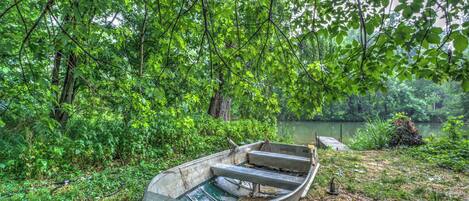 Un bote a remeros llamado 'Crackbill Farm' sobre una orilla cubierta de césped, junto a una masa de agua tranquila, rodeado de frondosa vegetación verde.