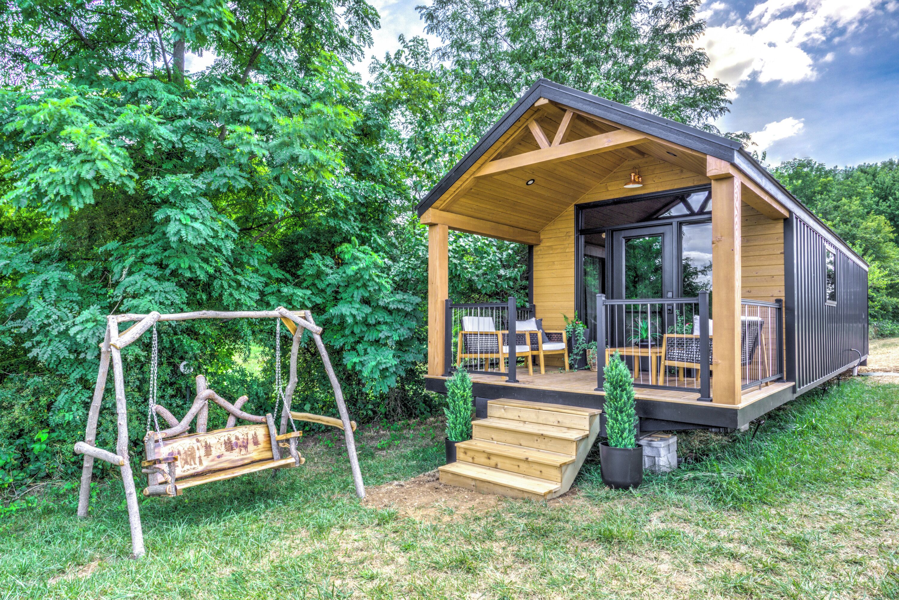 Une cabane en bois avec une véranda, une balançoire et un petit escalier menant à l’entrée.