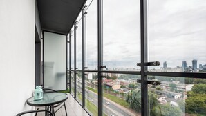 A balcony with a glass table and chairs, overlooking a cityscape with roads and buildings. - Prymasa Tysiąclecia Comfort Apartment (Warszawa)