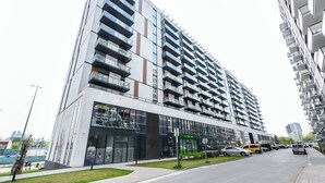 A modern high-rise building with multiple balconies, a glass facade, and a parking area with cars. - Prymasa Tysiąclecia Comfort Apartment (Warszawa)