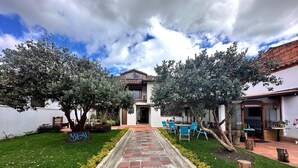 A hotel entrance with a paved pathway leading to a seating area, surrounded by trees and a well-maintained lawn. - BLAU HOTEL CAFE (Sopó)