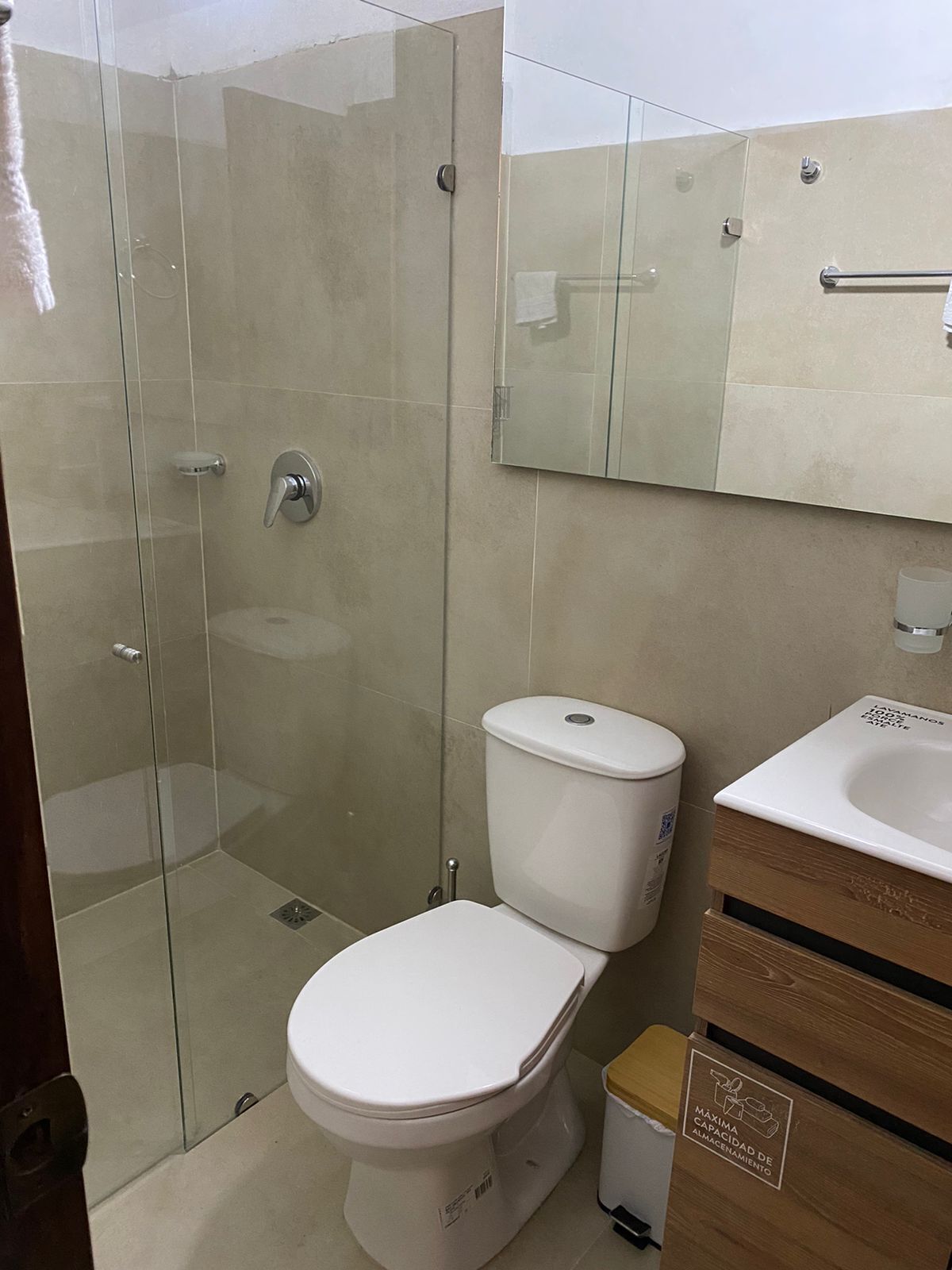 Un baño moderno con ducha de vidrio, inodoro blanco y tocador de madera con lavamanos.