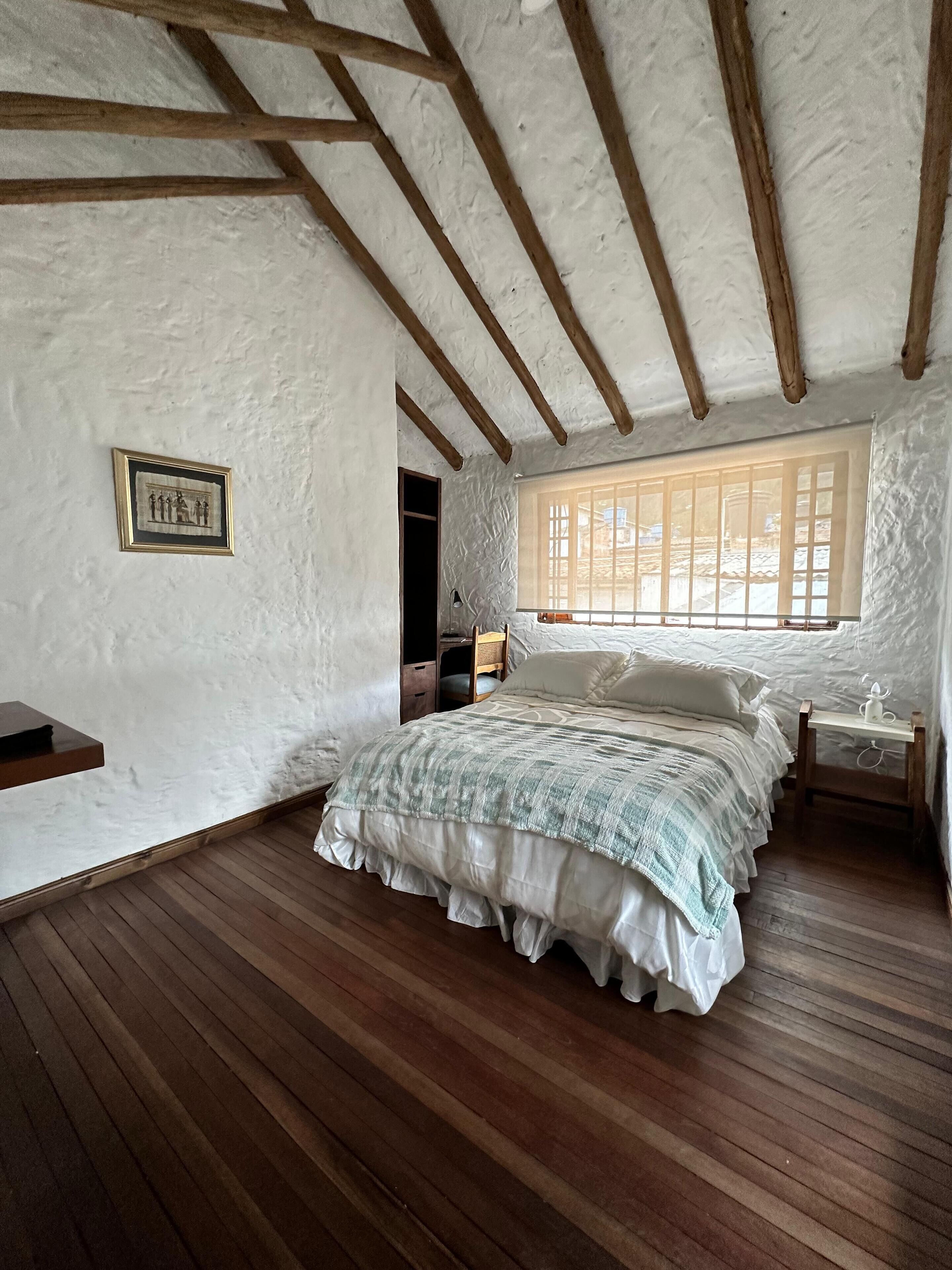 A bedroom with a wooden bed, white walls, a framed picture, and a window with bars.