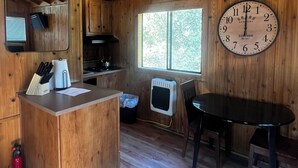 A wooden cabin interior with a kitchen area, a dining table, and a large wall clock. - Secluded Nature Escape, Pet Friendly with WiFi in Three Rivers (Three Rivers)