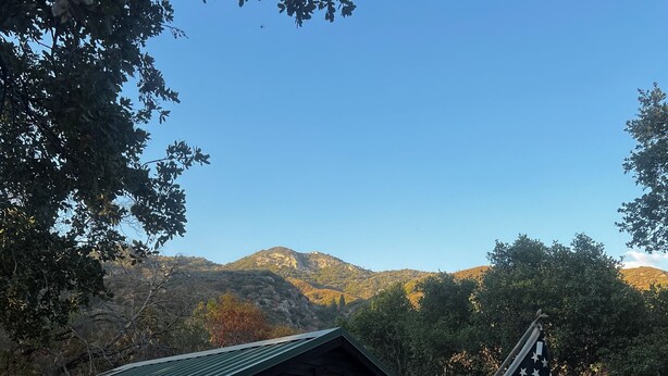 A rustic cabin with a metal roof, a patio with chairs and a table, an American flag, and a view of mountains in the background. - Secluded Nature Escape, Pet Friendly with WiFi in Three Rivers (Three Rivers)