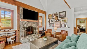 A cozy living room with a stone fireplace, leather furniture, and a variety of framed pictures on the walls.