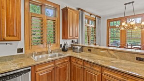 A kitchen with wooden cabinets, a granite countertop, a stainless steel sink, a toaster, and a chandelier.