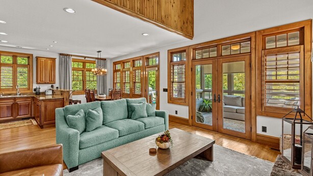 A spacious living room with a green sofa, wooden coffee table, and large windows offering views of greenery.
