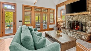 A spacious living room with a stone fireplace, a large TV mounted above it, and a cozy seating area with a green sofa.