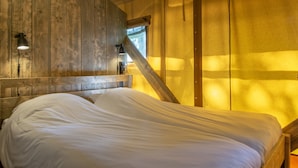 A bed in a room with wooden walls and a sloped ceiling. - Safari Tent in Holiday Park (Arcen)