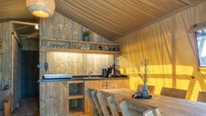 A rustic wooden interior with a wooden dining table, chairs, and a kitchen area with a built-in shelf. - Safari Tent in Holiday Park (Arcen)