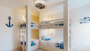 Dormitorio con literas, ventilador de techo, repisas en la pared y decoración temática náutica.
