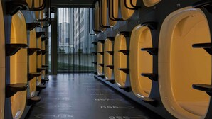Une rangée de fenêtres rondes, teintées de jaune, portant des numéros indiquant le numéro des chambres, mène à une porte qui donne sur une vue panoramique de la ville.