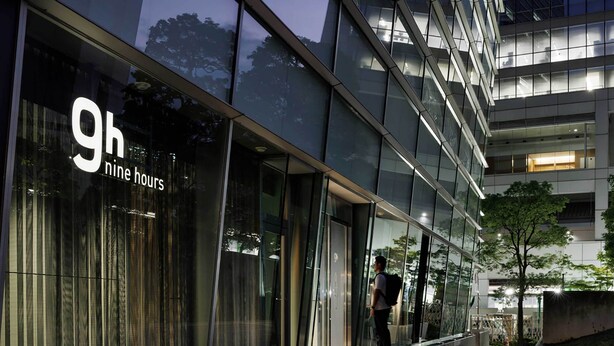 Un bâtiment moderne doté de grandes fenêtres en verre et d’une enseigne indiquant « 9h – neuf heures ».