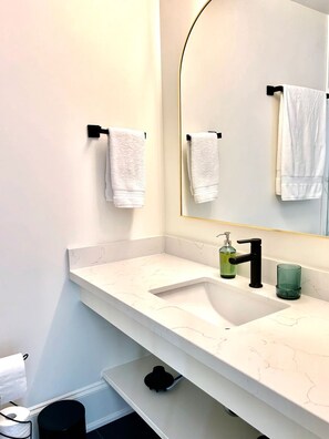 Een moderne badkamer met een witte marmeren wastafel, een zwarte kraan en een grote spiegel.