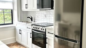 A modern kitchen with white cabinets, a stainless steel refrigerator, a built-in oven, and a microwave.