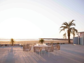 A patio with wicker chairs and a table, overlooking a beach with palm trees and a clear sky. - Sugar Beach Oarai (Oarai)
