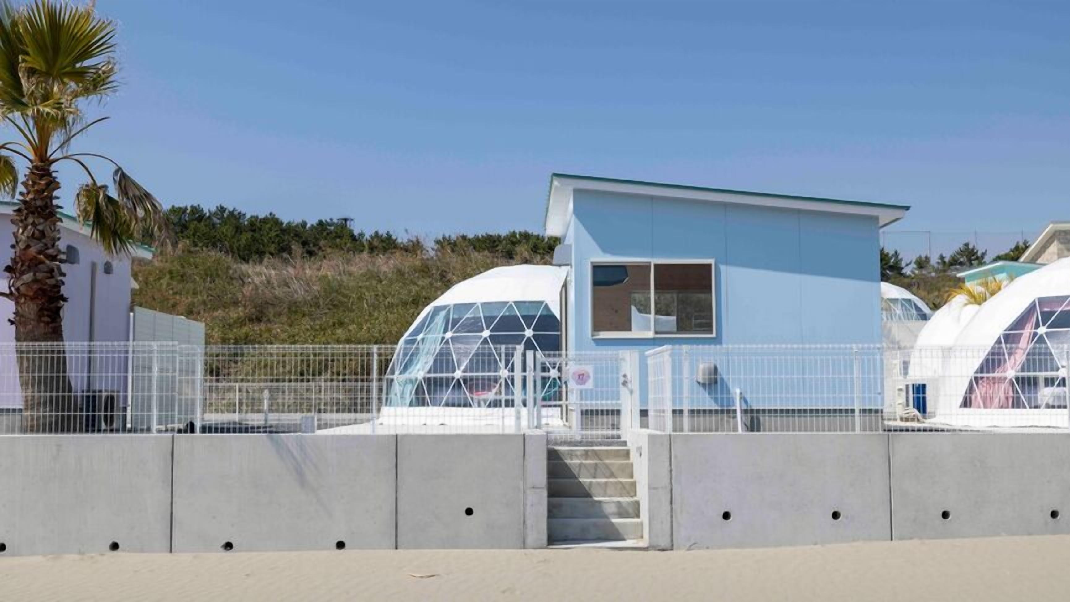 A modern building with a blue exterior, a small window, and a staircase leading to a door.