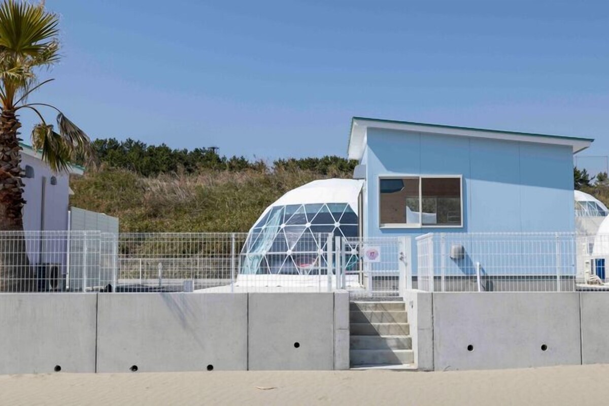 A modern building with a blue exterior, a small window, and a staircase leading to a door.