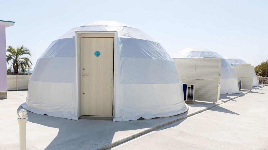 A series of dome-shaped yurts with a door, each covered with a white tarp, on a flat rooftop.