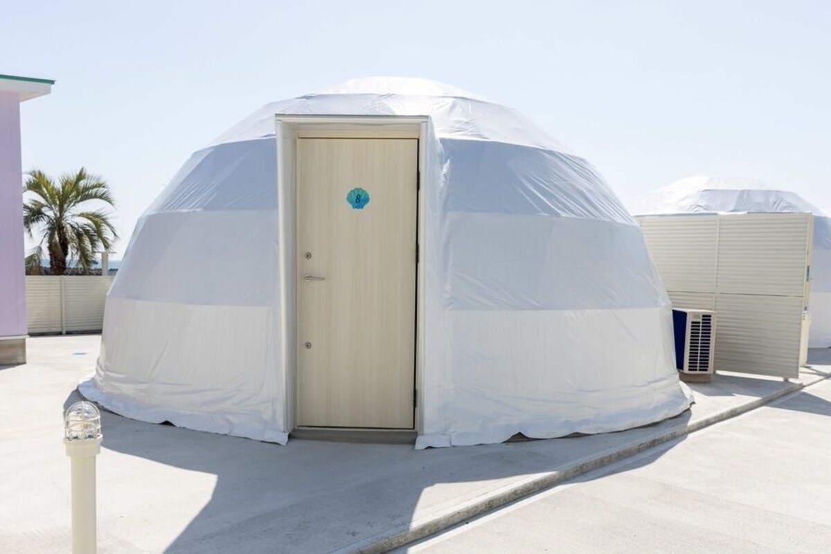 A series of dome-shaped yurts with a door, each covered with a white tarp, on a flat rooftop.