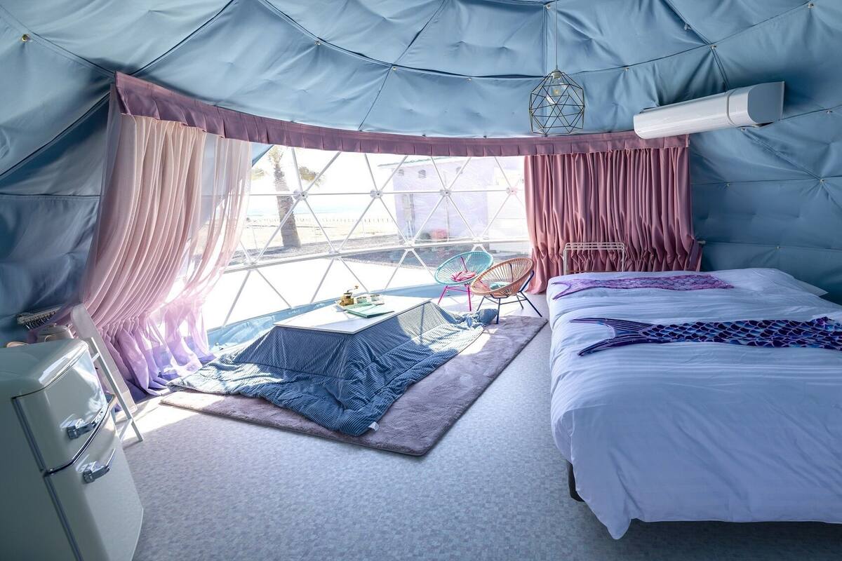 A tent-style room with a bed, a chair, a small table, and a window.