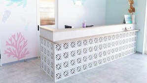 Egy fehér és világoskék színvilágú recepciós pult, egy dekoratív, sellőket ábrázoló falfestmény és egy egyszerű, modern dizájn.