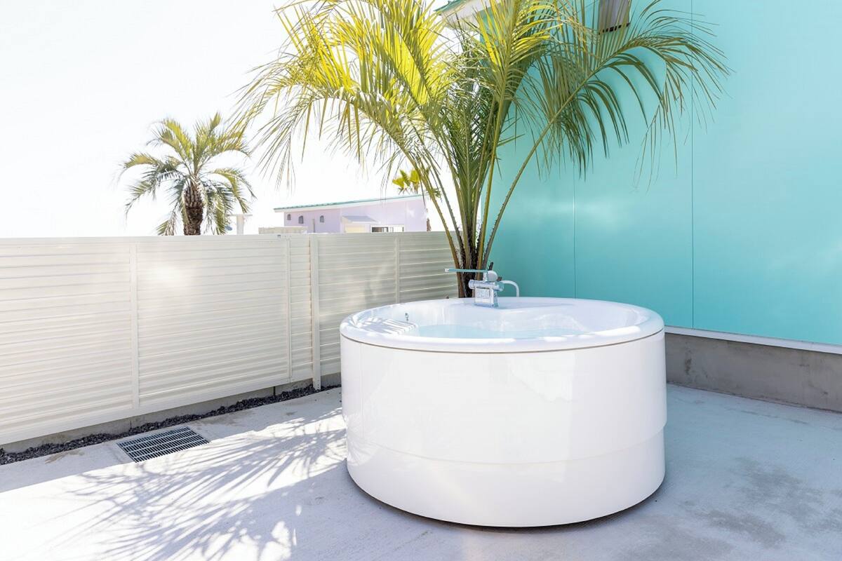 A hot tub on a rooftop with a view of a teal building and palm trees.