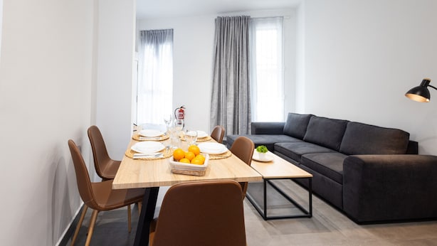Een moderne woonkamer met een eethoek. Er is een bank, een eettafel met stoelen en een kleine plant op de tafel.